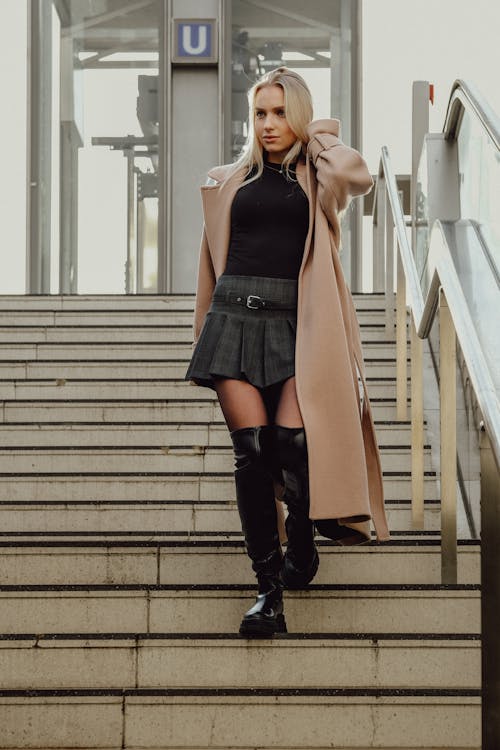 Blonde Woman in a Coat, a Skirt and Boots Walking Down the Stairs
