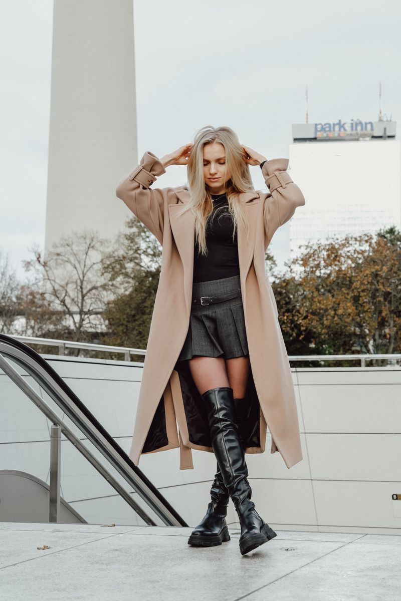 woman in oversized trench coat with mini skirt and knee-high boots