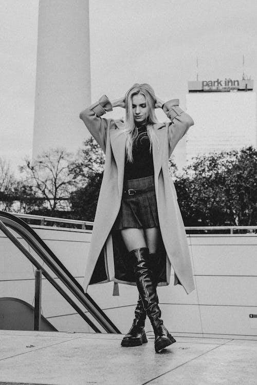 Woman in a Coat and Boots Standing with her Hands in her Hair