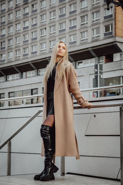 Blonde Woman in a Coat and Boots Leaning on a Railing