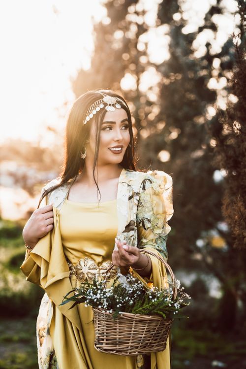 Free Elegant woman in a yellow sari with floral basket in a sunlit outdoor setting. Stock Photo