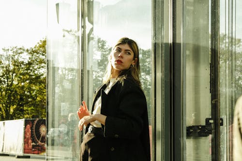 Model in a Black Wool Coat and a White Sweater Leaning Against the Glass Wall of an Elevator