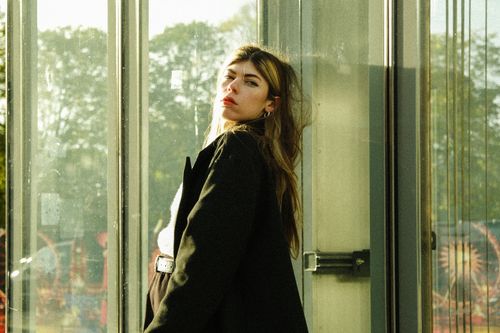 Free Stylish woman in a black coat posing against a modern glass backdrop in urban setting. Stock Photo