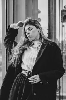 Stylish woman poses in urban setting wearing a coat in a black and white portrait.