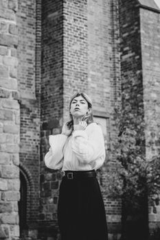 Stylish black and white photo of a woman posing in front of a textured brick building, blending elegance and architecture.