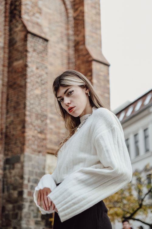 Free Stylish woman in a white sweater poses confidently against a redbrick background. Stock Photo