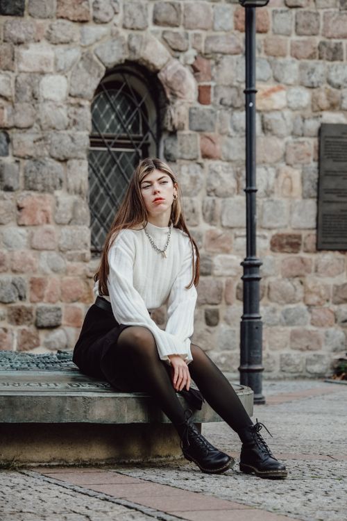 Free A young woman poses stylishly by a historic brick building, showcasing modern fashion. Stock Photo