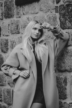 Black and white portrait of a woman in a wool coat posing against a stone wall.