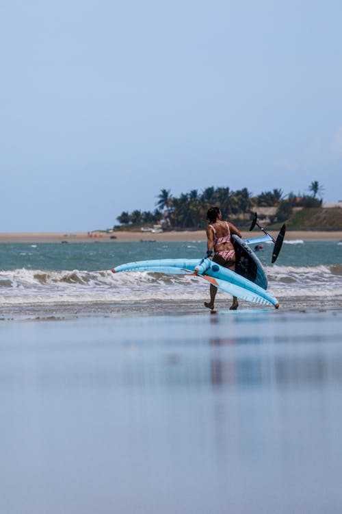 Surfer Carrying a Foilboard and a Wing Along the Beach to the Sea
