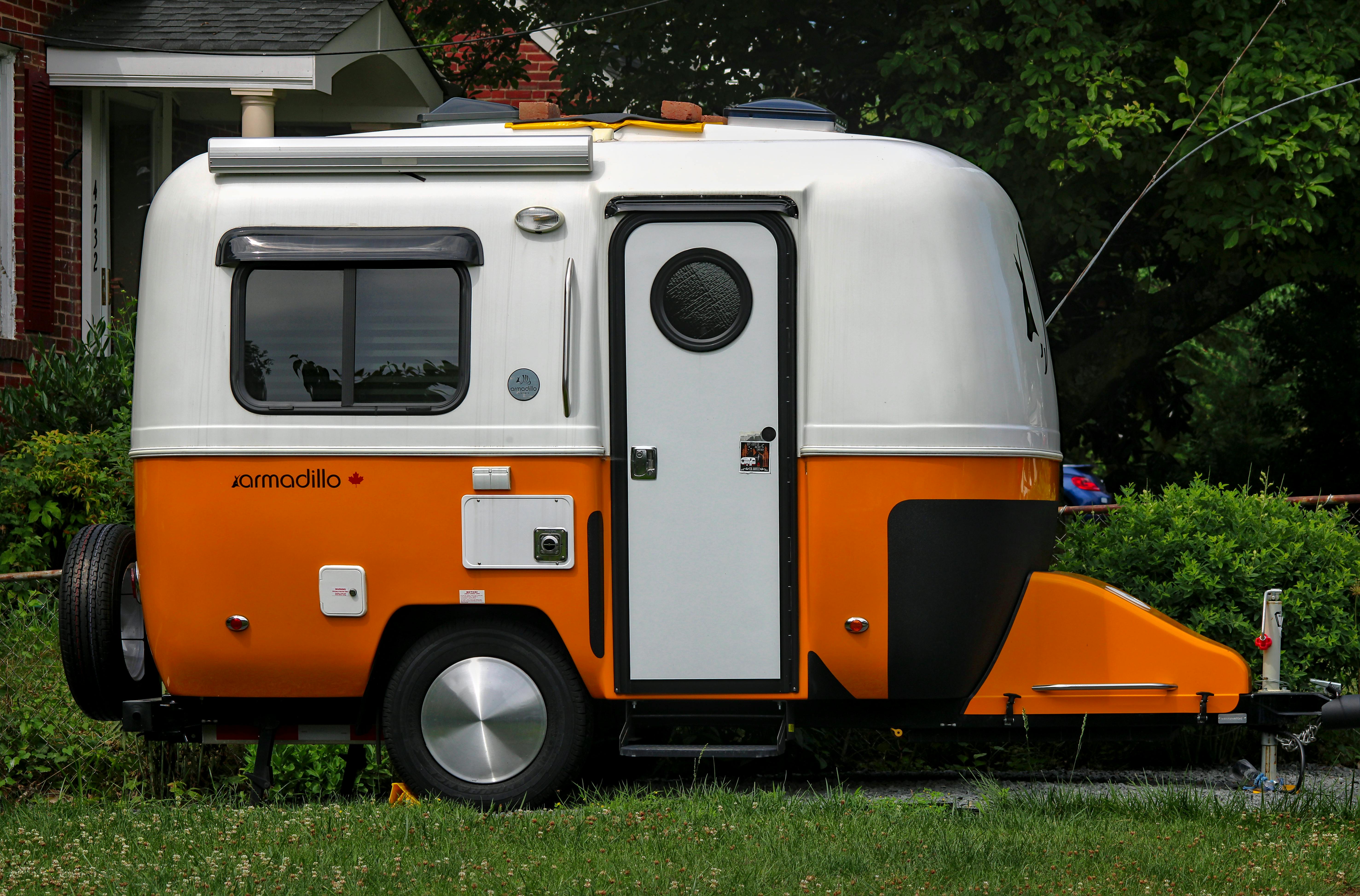 A bright orange and white Armadillo trailer parked in a suburban yard, surrounded by greenery.