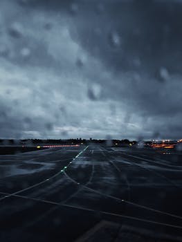 Moody view of Kastrup Airport runway in rain with dark clouds and wet asphalt creating a dramatic evening landscape.