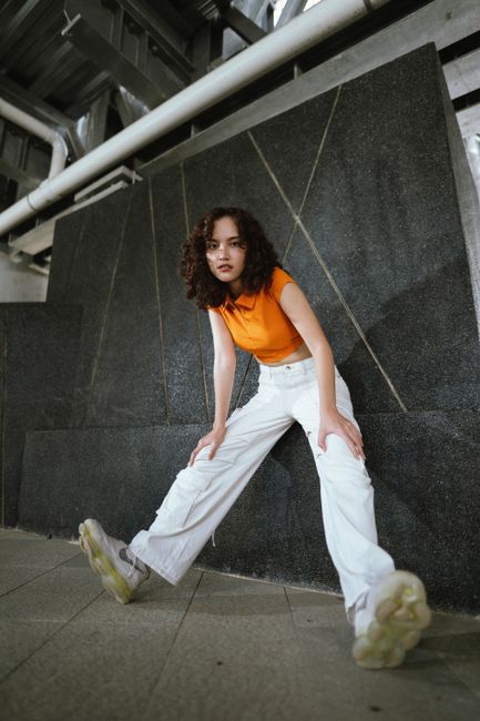 Stylish curly-haired model poses in vibrant urban setting, exuding confidence.