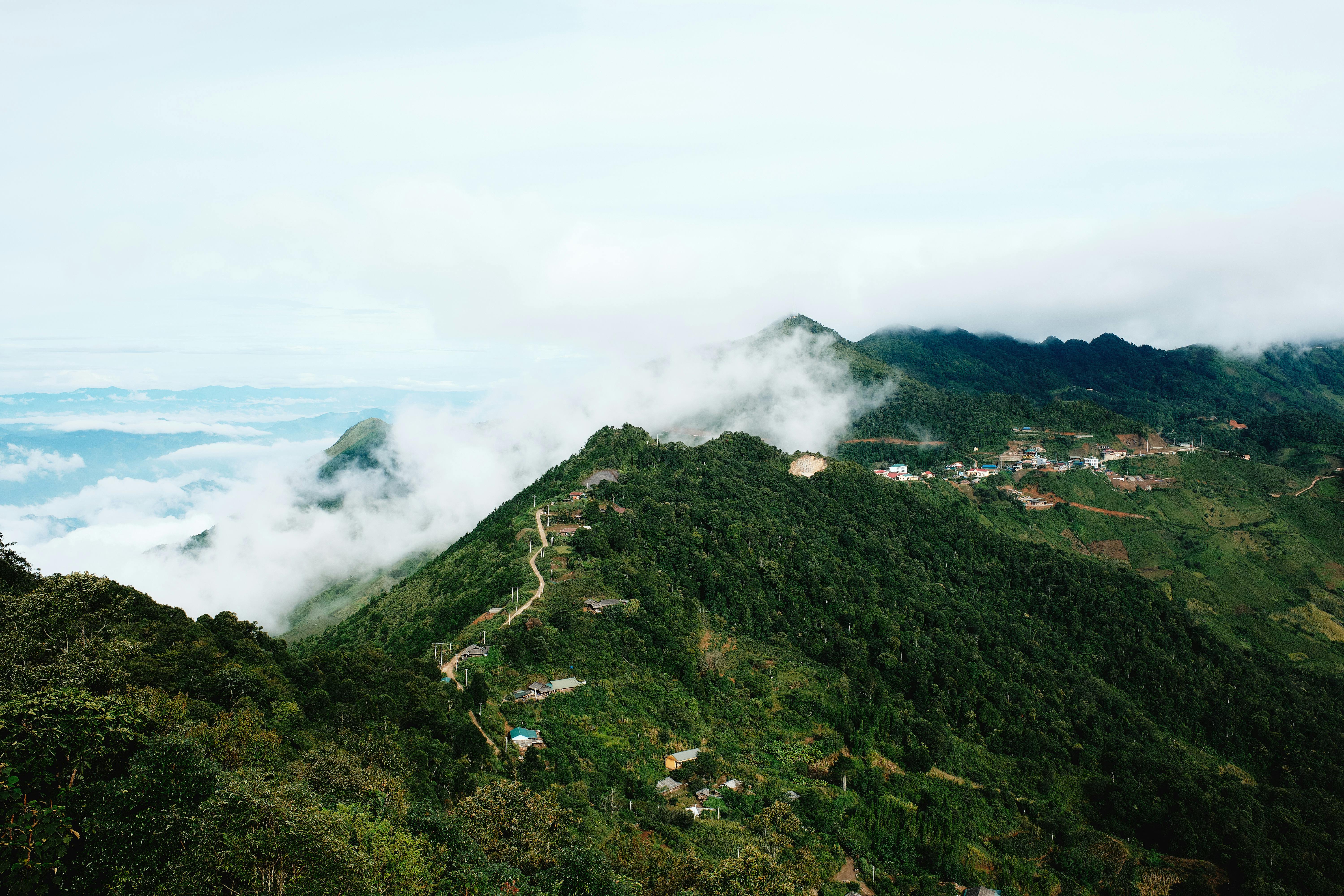 Breathtaking view of cloud-kissed mountains with lush green forests and fog enveloping the landscape.