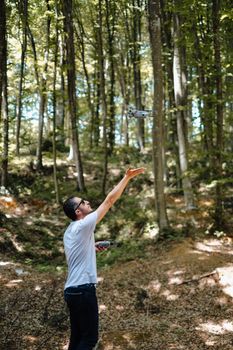 A man operating a drone in a lush İstanbul forest with sunlight filtering through the trees.