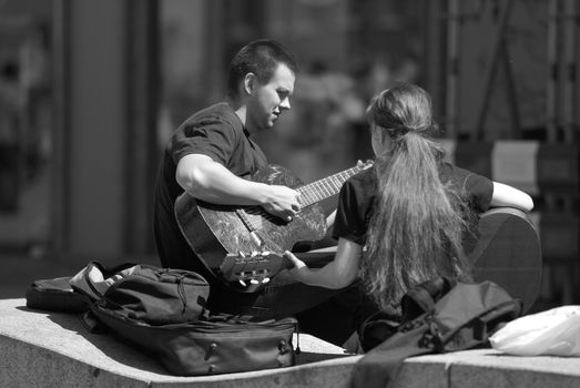 A man and a woman playing guitar on a bench