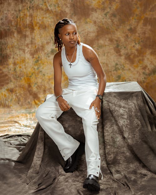 Woman in White Top and Pants Sitting on Box in Studio