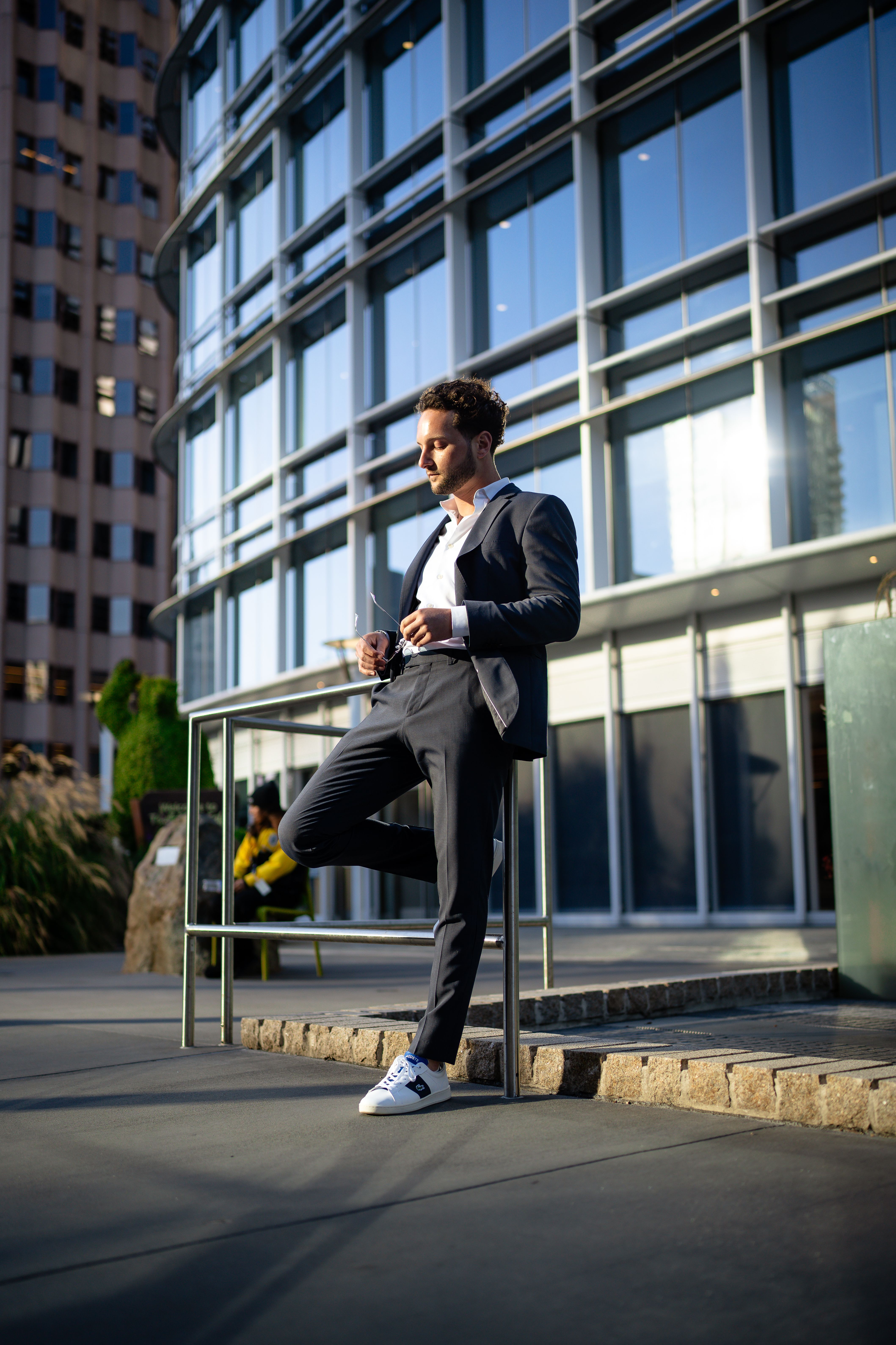 Stylish man in a blue suit poses outdoors against a modern cityscape, exuding urban elegance.