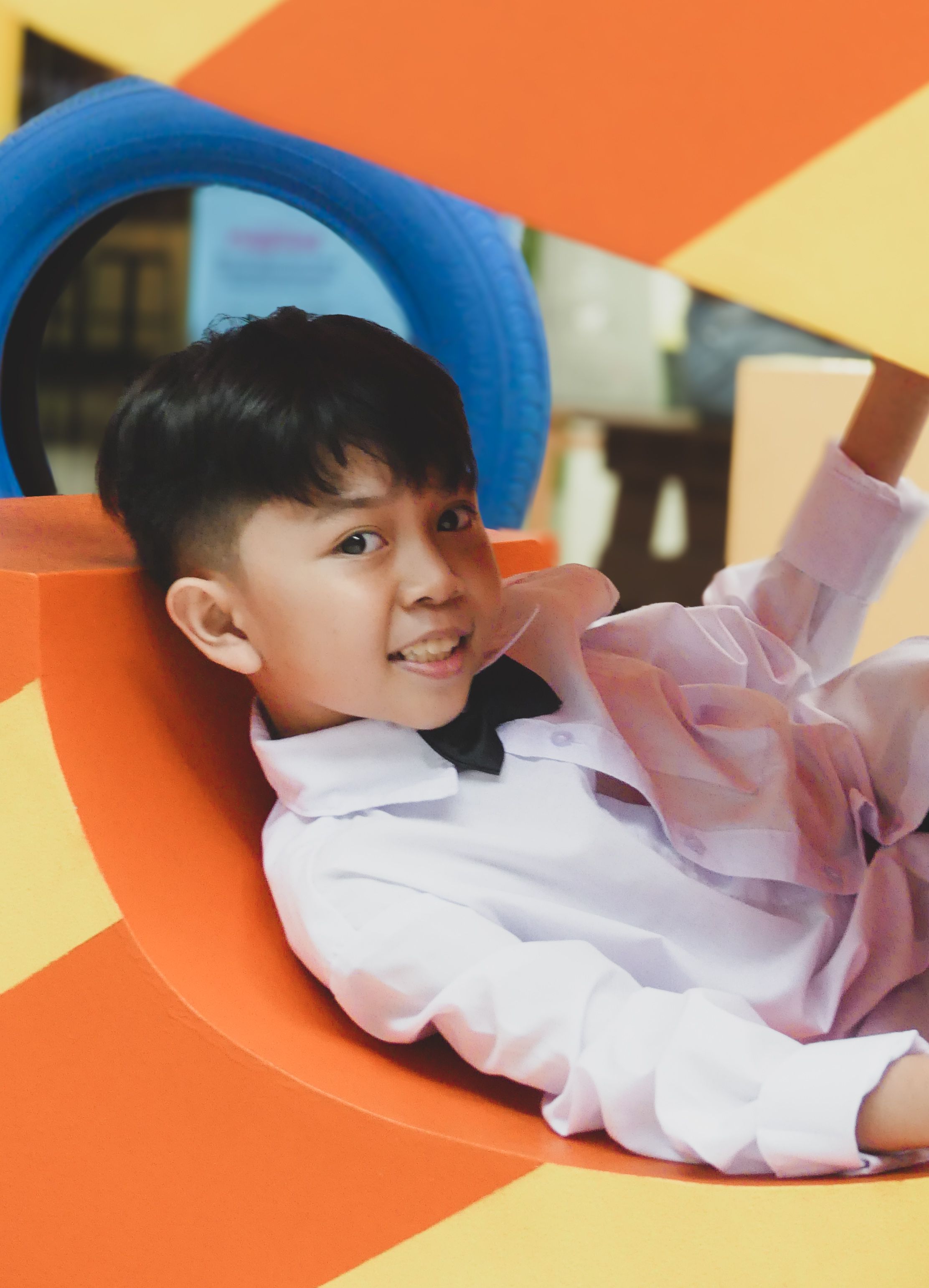 Asian boy having fun on a colorful playground in the Philippines, smiling inside a tunnel.