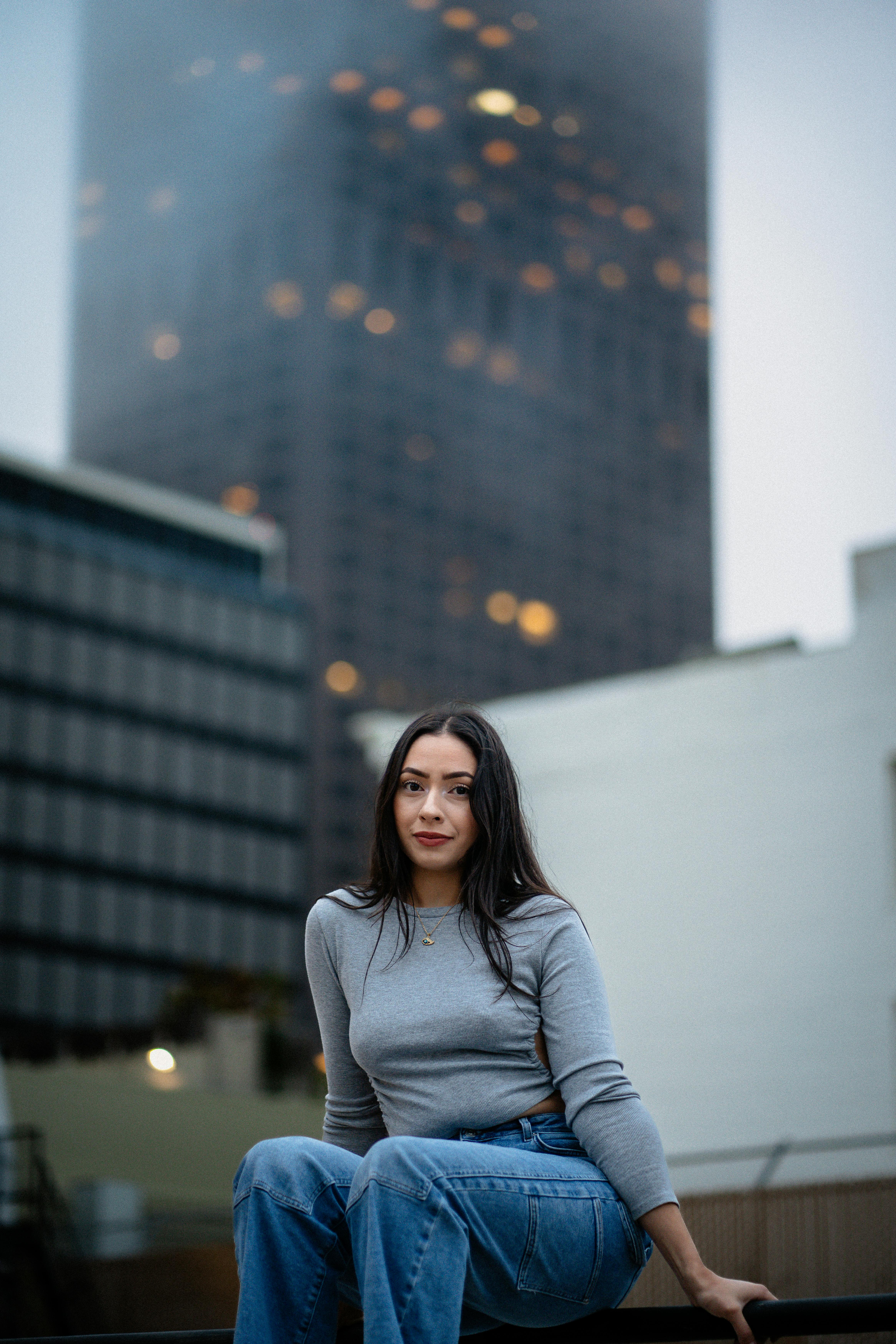 A woman poses in an urban setting with a skyscraper in the background.