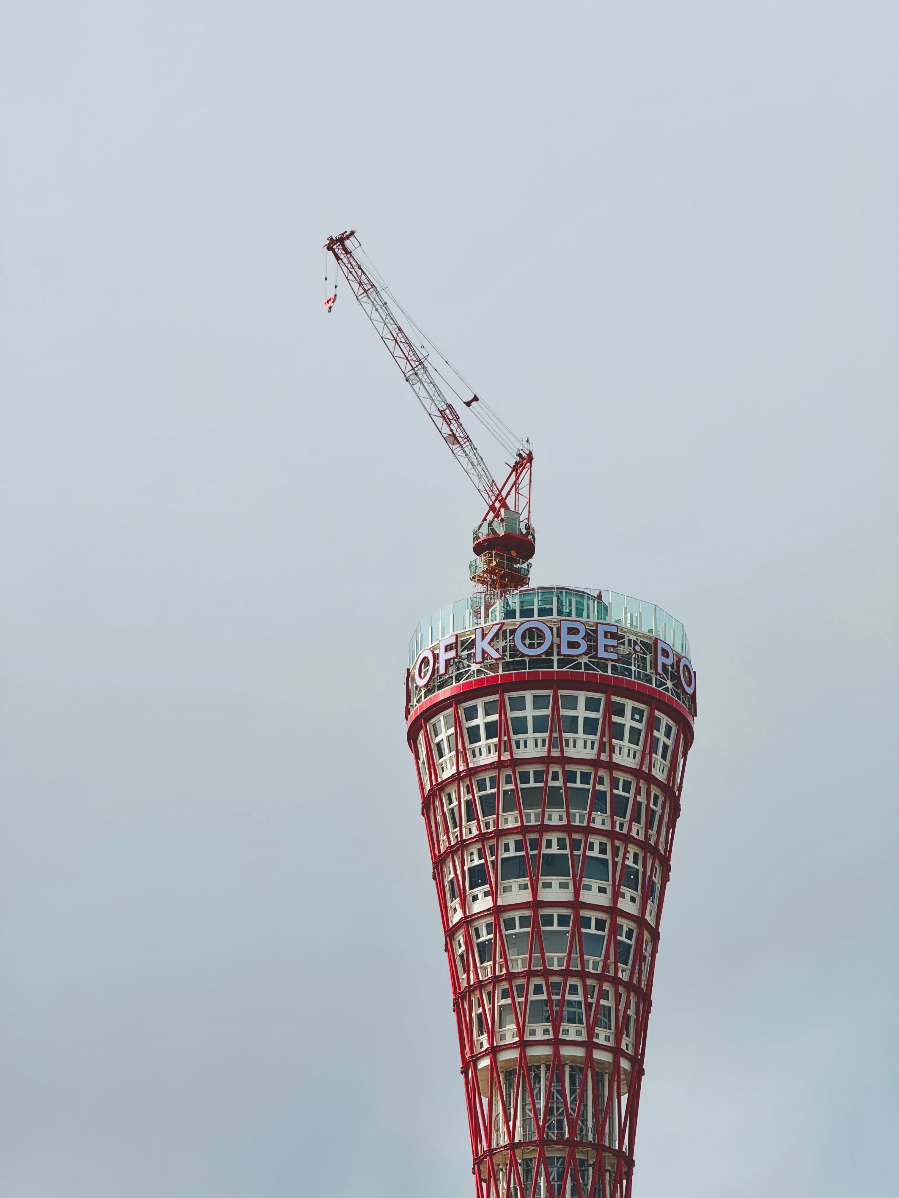 View of Kobe Port Tower with a construction crane set against an overcast sky in Kobe, Japan.