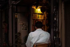 A man in a white shirt sits on a chair inside a warm, inviting bookstore at night.