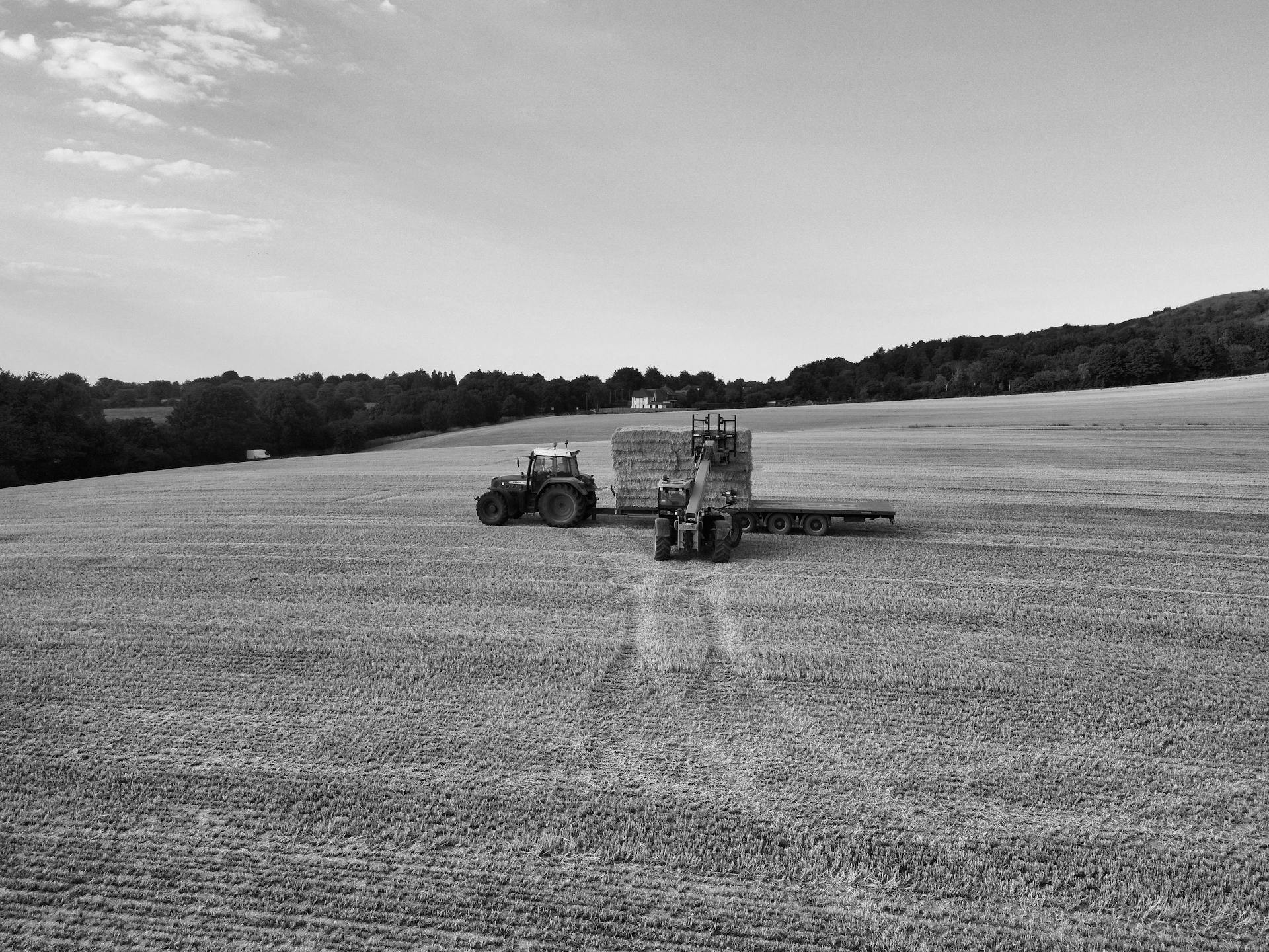 Aerial view of tractors on a rural English field harvesting hay bales, showcasing agricultural machinery.