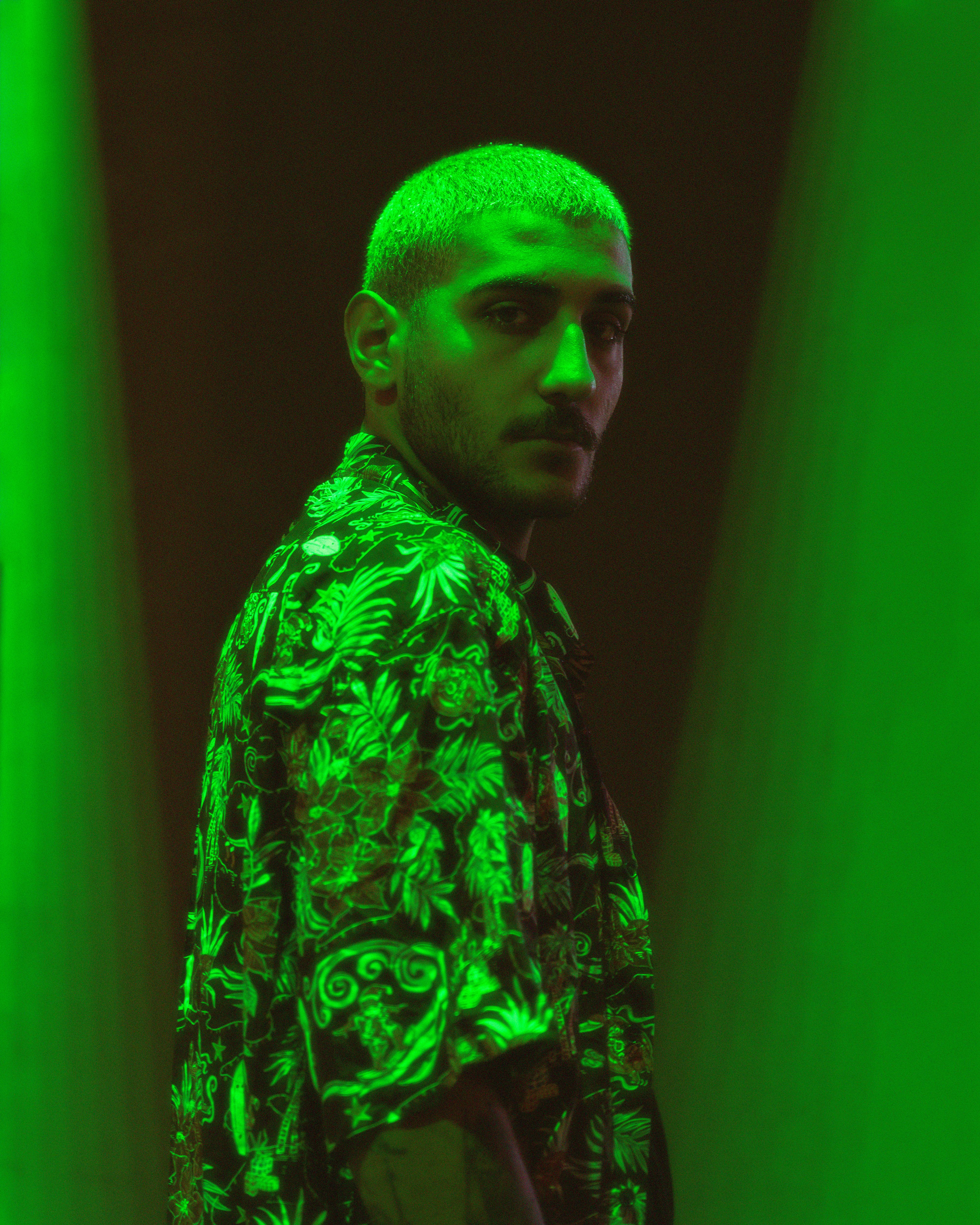 Stylish portrait of a man with short hair under dramatic green lighting.