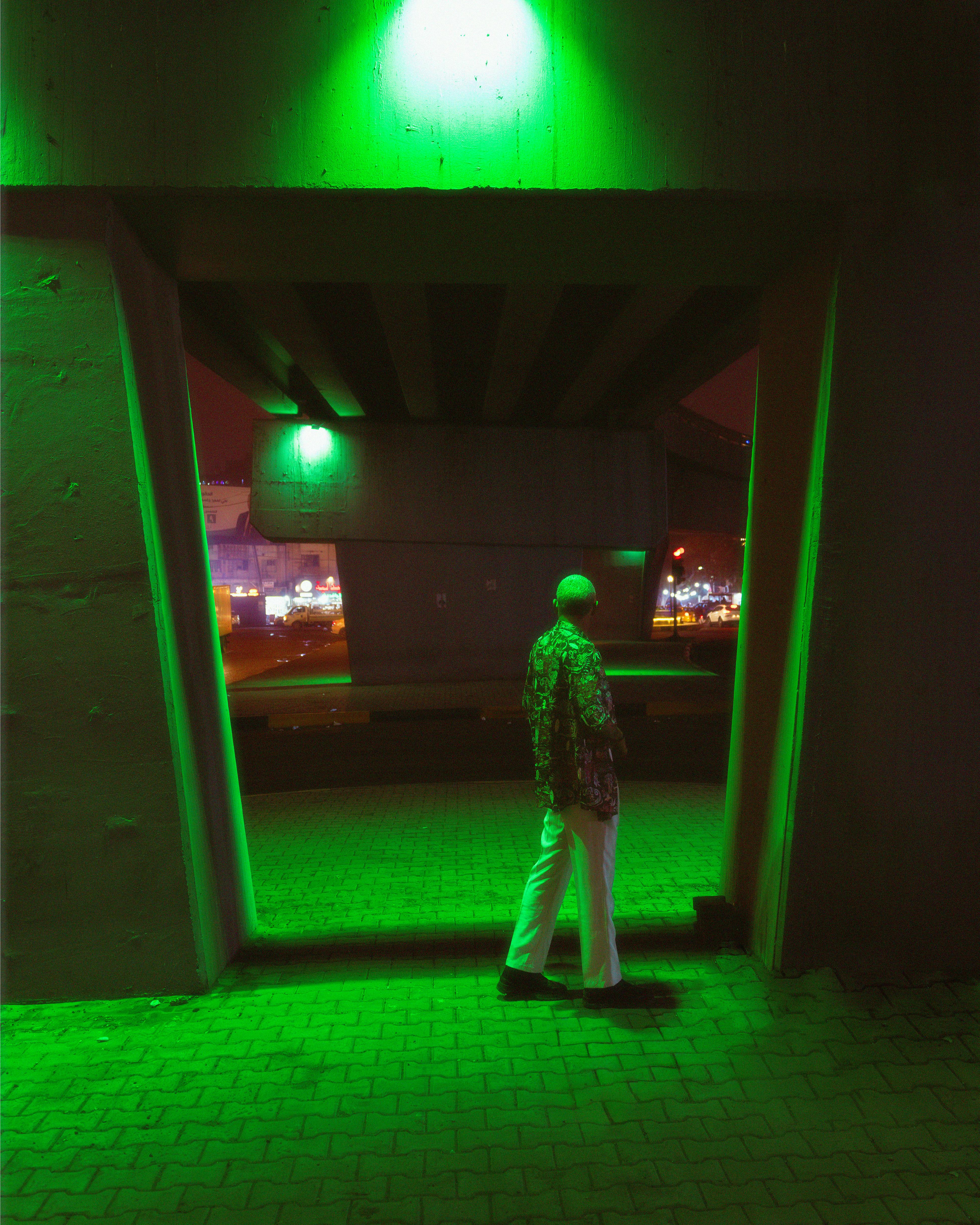 A person in motley attire stands under an illuminated urban bridge at night.