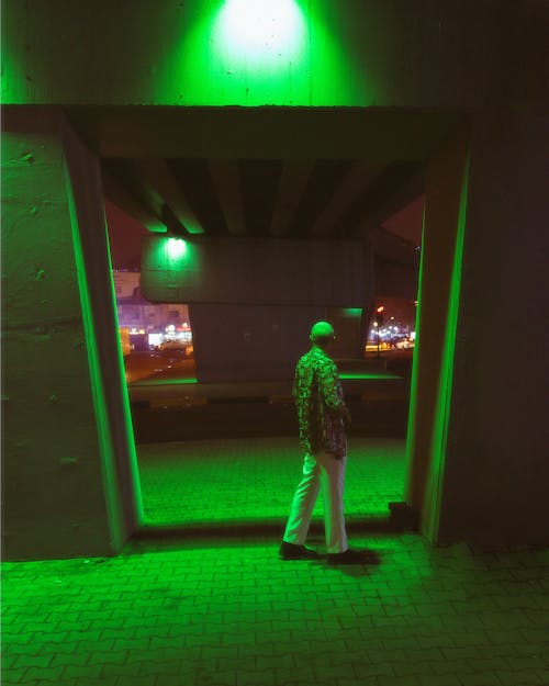 Man in a Motley Shirt Standing under a Bridge Illuminated by Green Light