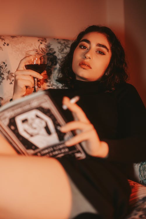 Woman Smoking while Sitting in Armchair with Book and Wine Glass