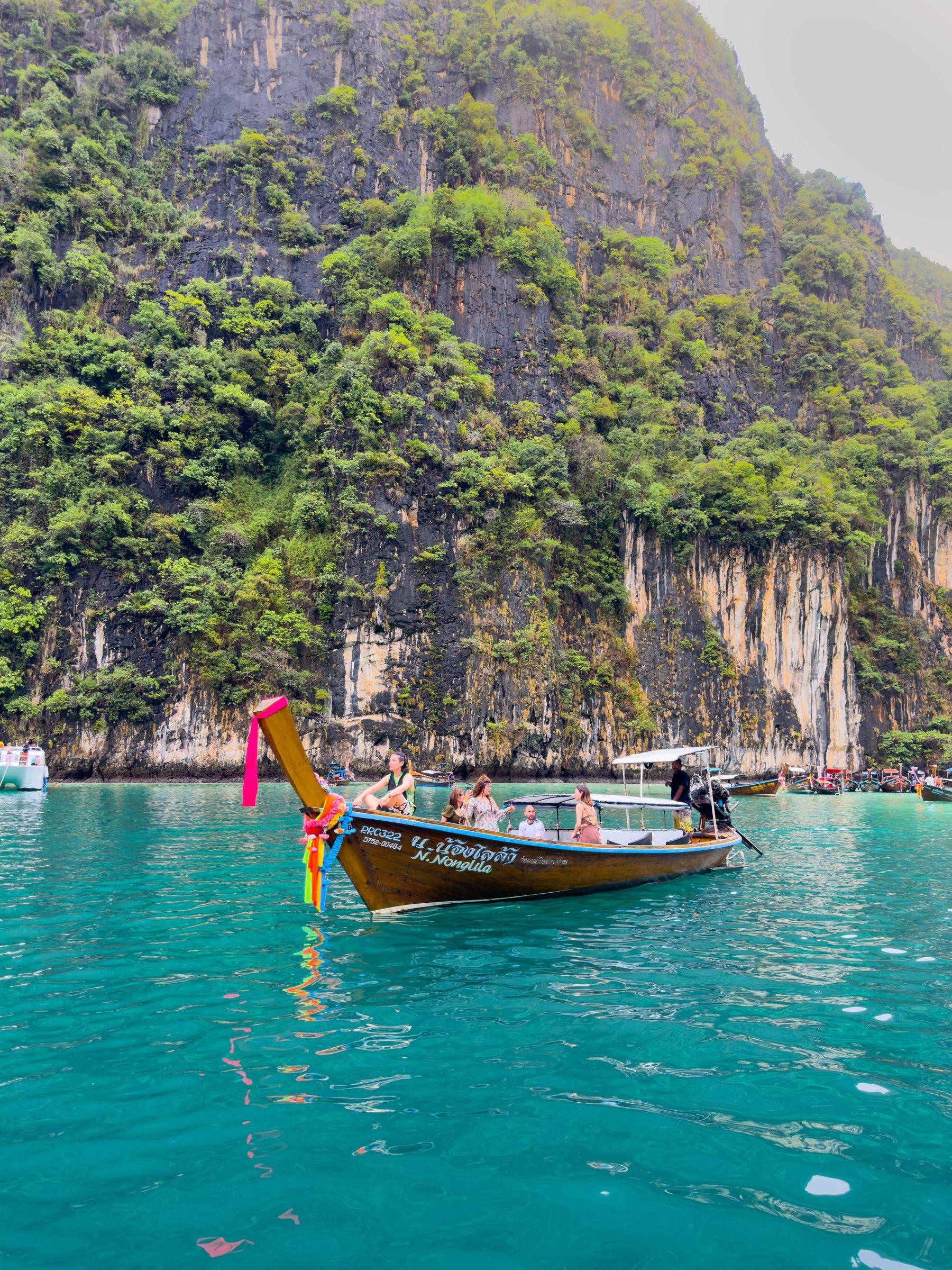 Travelers aboard a Thai longtail boat beneath Phi Phi limestone cliffs