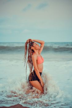 A young woman with braided hair posing in swimwear in the ocean waves on a sunny beach day.