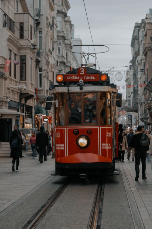 Free Iconic red tram navigating a lively street in Istanbul's Taksim area with commuters and pedestrians. Stock Photo