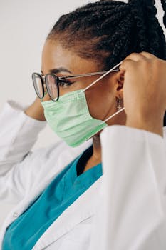 A healthcare professional in scrubs and a mask adjusts her protective gear, showcasing safety and preparedness.
