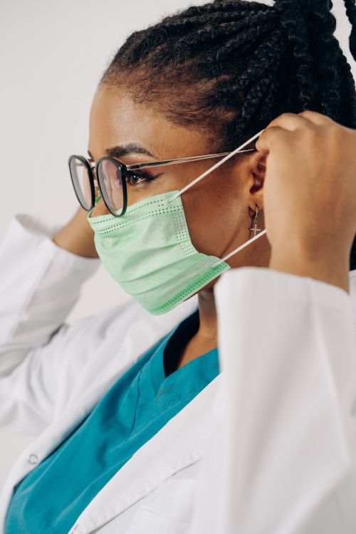 Free A healthcare professional in scrubs and a mask adjusts her protective gear, showcasing safety and preparedness. Stock Photo