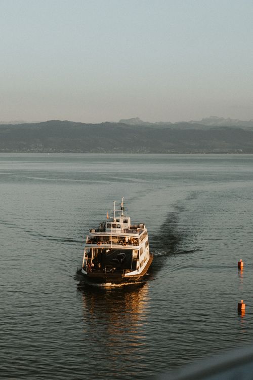Free A ferry travels across a calm lake surrounded by mountains under a clear sky. Stock Photo