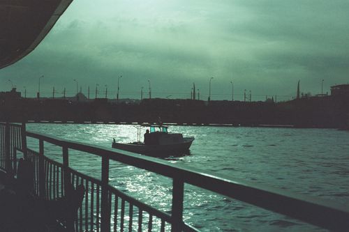 Free A motorboat glides through Istanbul's waters under a twilight sky, with city silhouettes and railings in view. Stock Photo