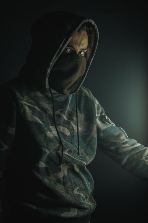 Free Portrait of a man with obscured face in a camouflage hoodie, creating a mysterious atmosphere. Stock Photo