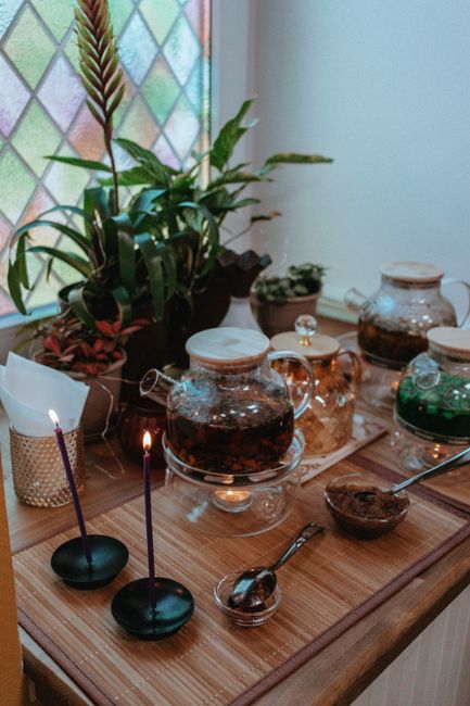 Pale yellow-green tea steeping in a glass teapot with loose tea leaves unfurling at the bottom, steam rising above a small ceramic cup beside it.