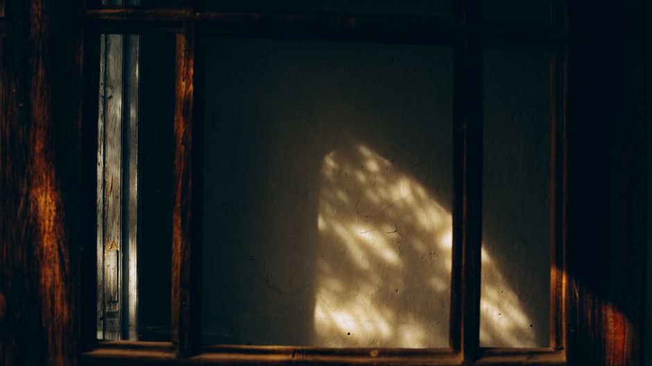 Dramatic indoor scene with light casting shadows through a rustic wooden window.