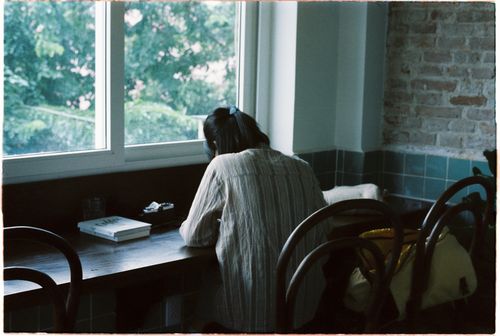 Free A woman sits by the window in a cozy cafe, absorbed in study. Warm and inviting atmosphere. Stock Photo