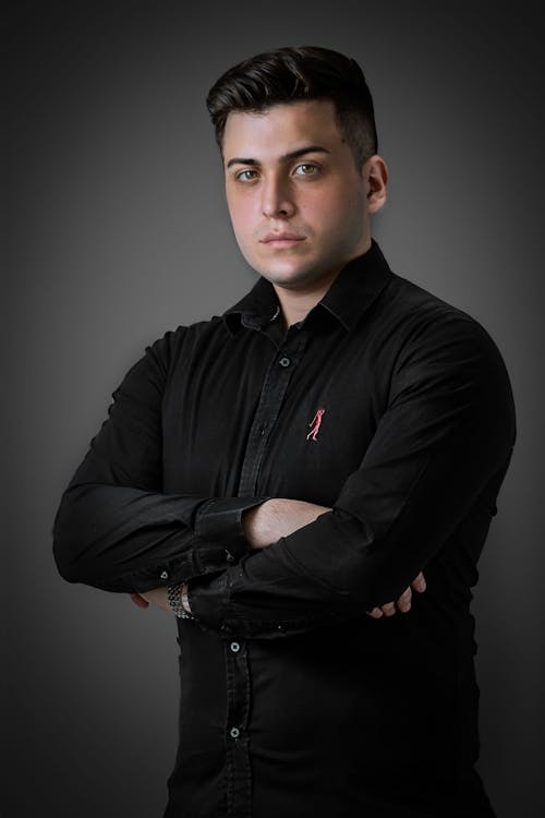 Studio Shot of a Young Man in a Black Shirt Standing with Arms Crossed 