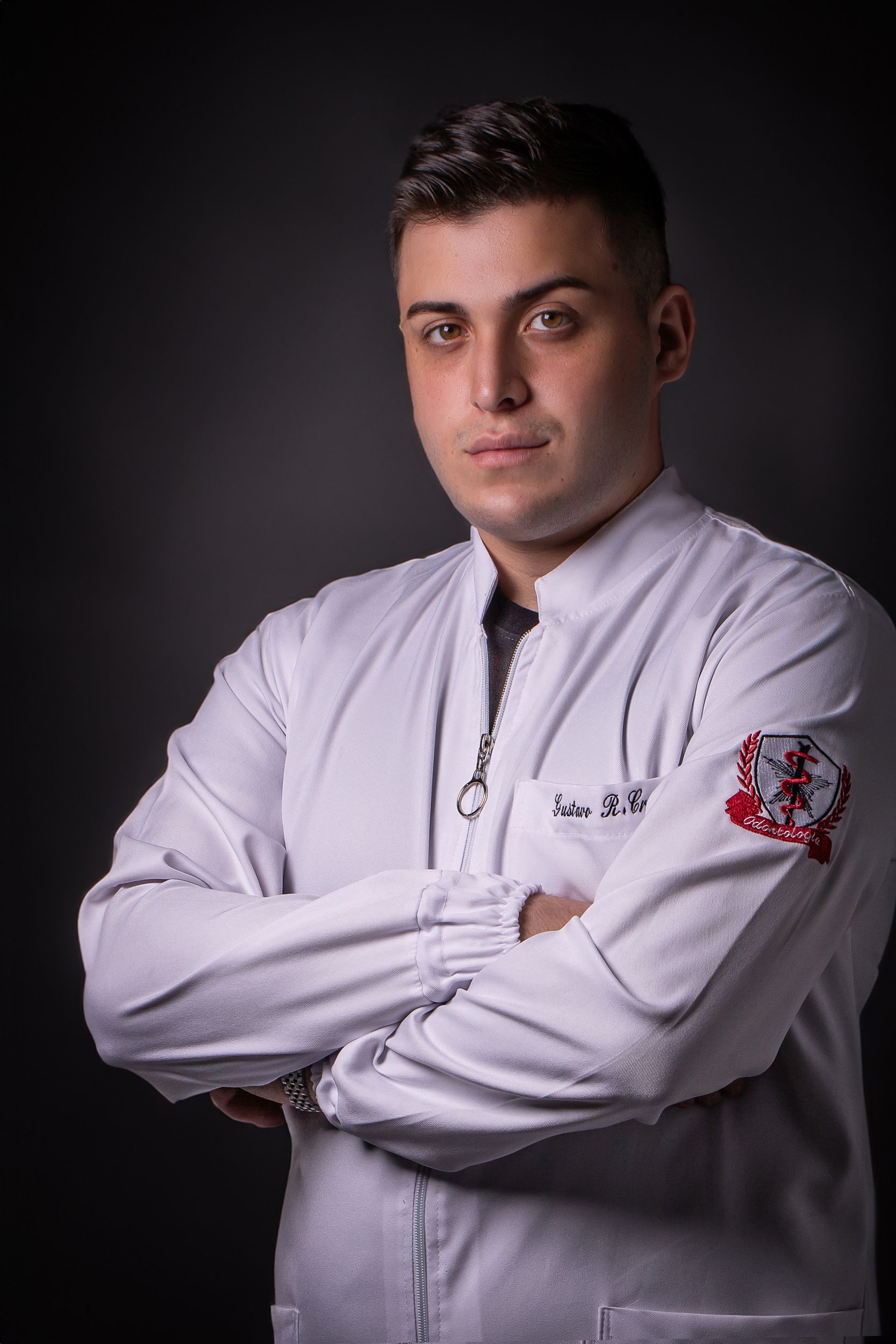 Portrait of a serious man in a white jacket with arms crossed, set against a gray studio background.