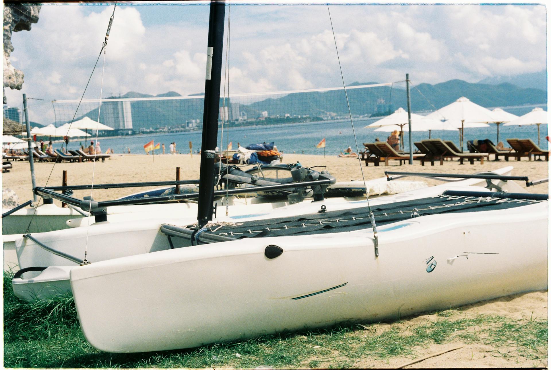 Catamarans on a sandy beach with sun loungers and umbrellas, perfect for a sunny summer day.