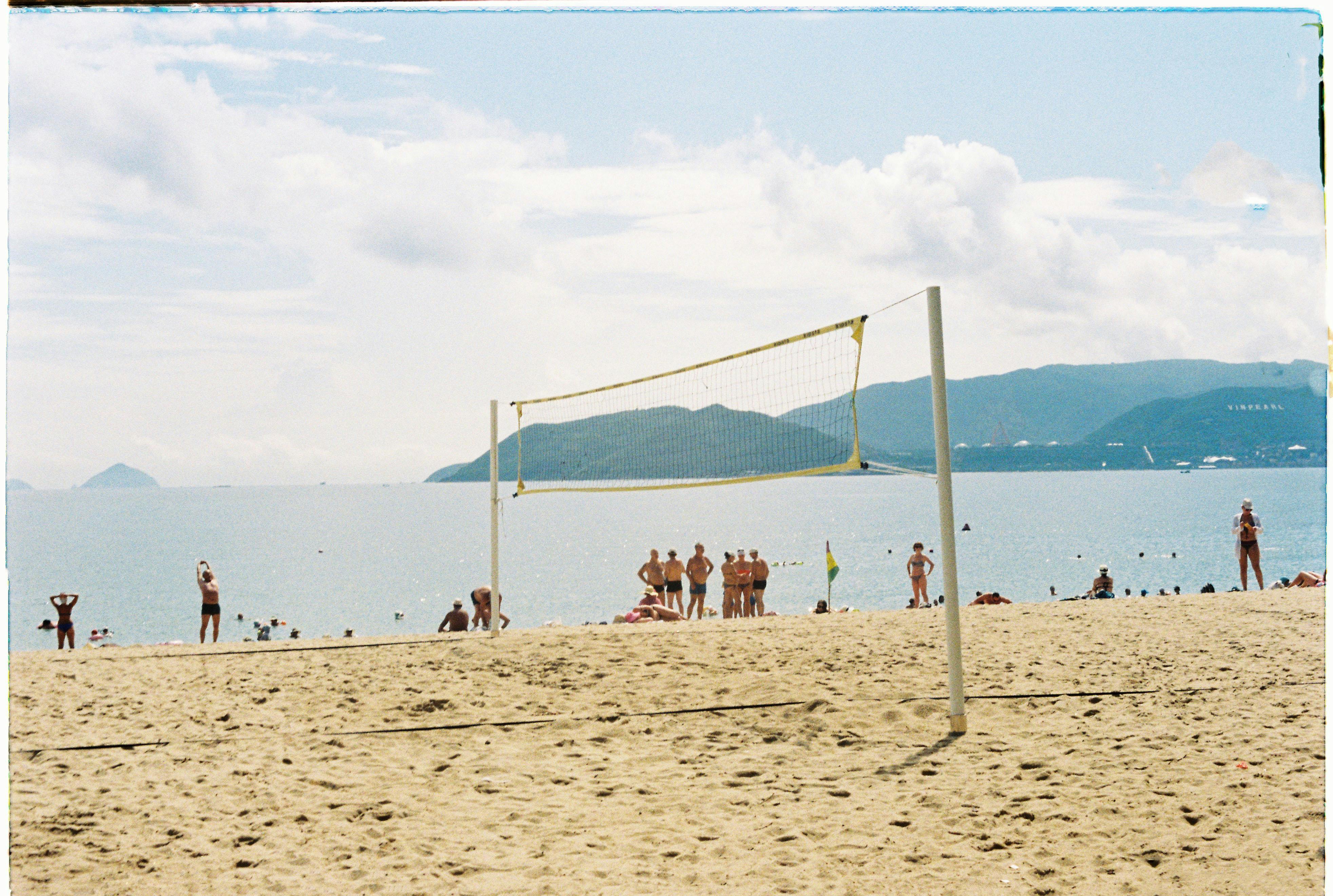 A vibrant beach scene with people playing volleyball by the sea under a sunny sky.