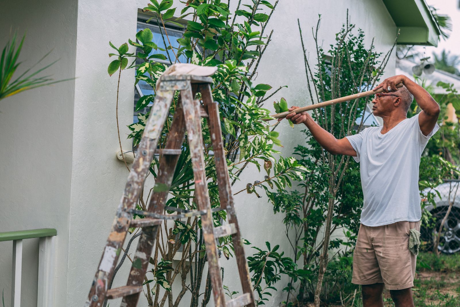Man painting the white stucco exterior of a house from a ladder
