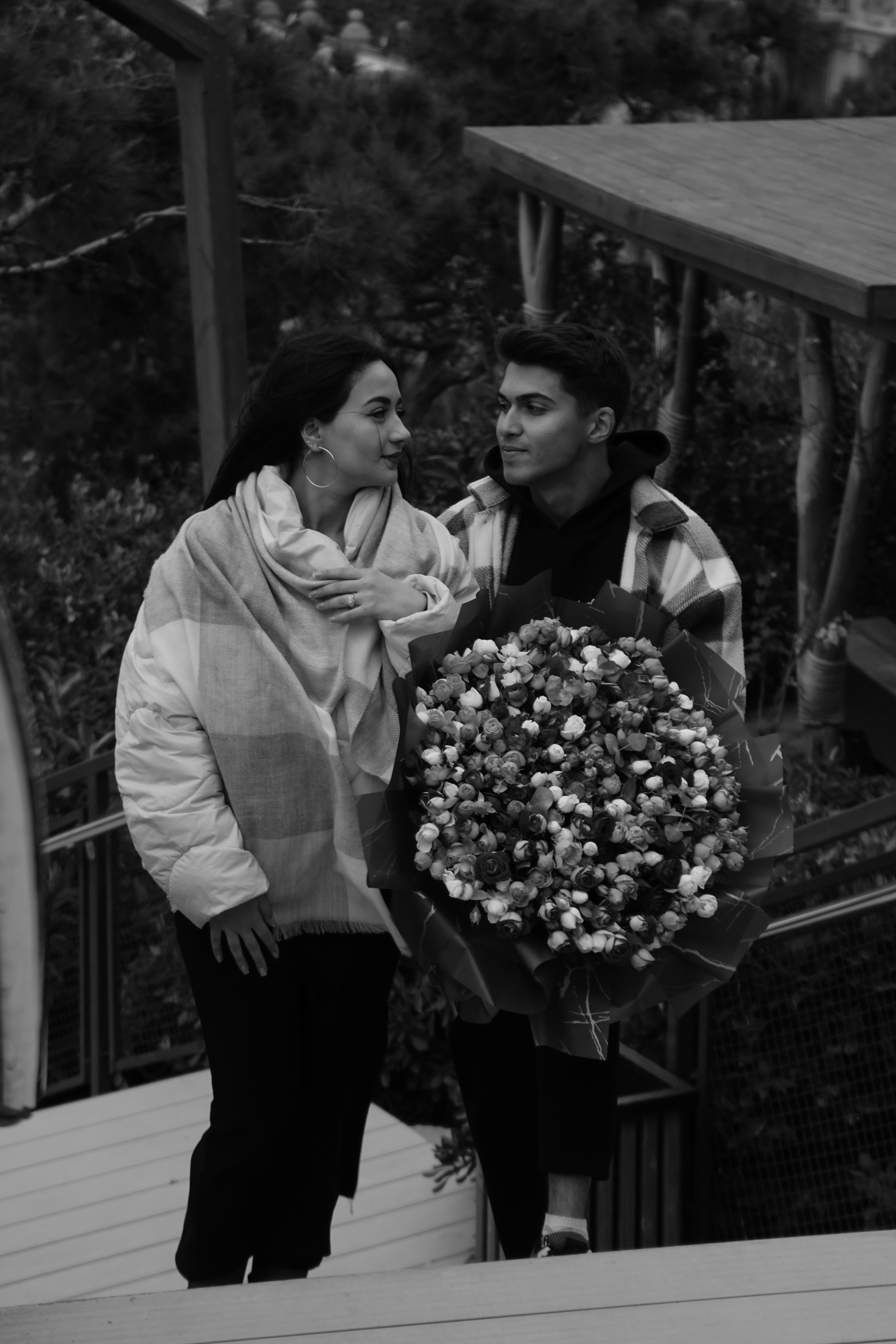A couple embracing with a bouquet on stairs in a park setting.