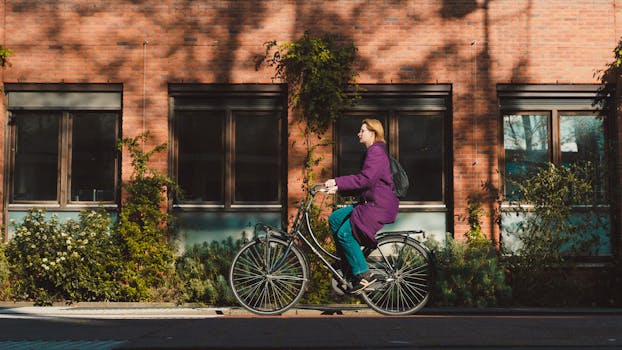 A woman in a purple coat rides a bicycle through Amsterdam's scenic streets on a sunny day.
