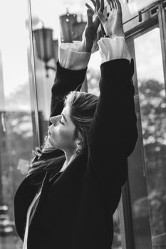 Black and white portrait of a young woman stretching with eyes closed, set against an urban backdrop.