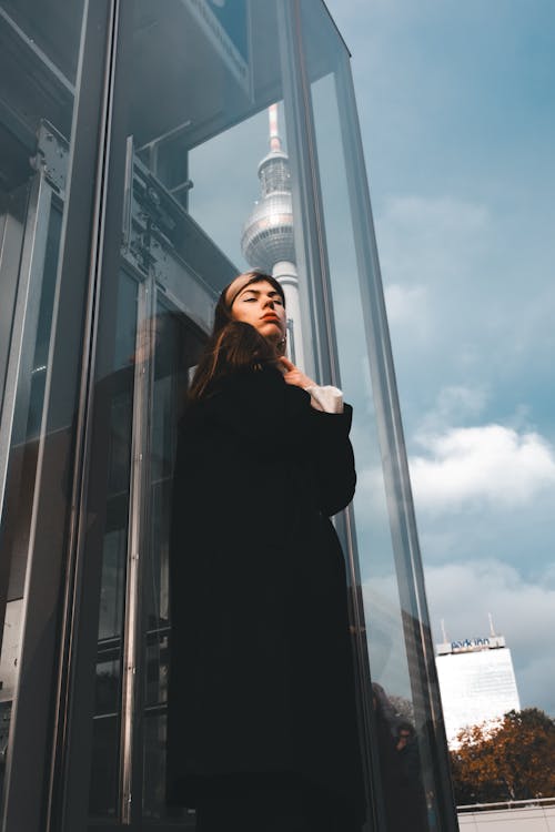 Low Angle Shot of a Young Woman in a Black Coat Standing by a Modern Building in City 
